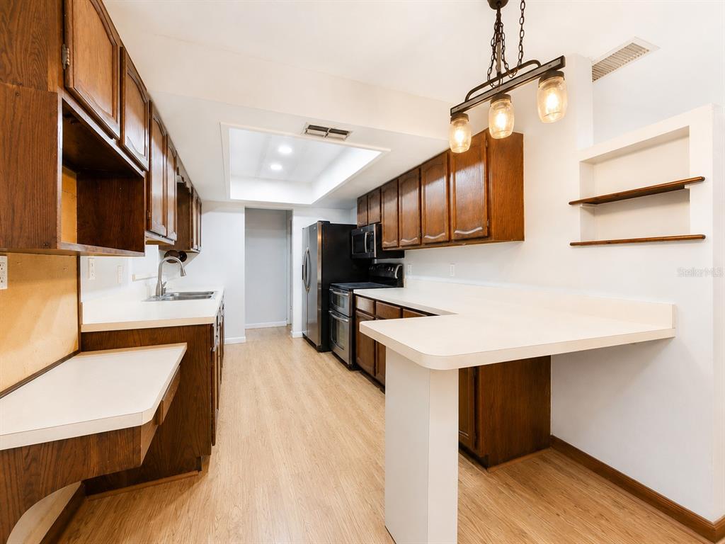 A kitchen features wood cabinets, white countertops, a breakfast bar, and stainless steel appliances — 5967 102ND AVENUE N, PINELLAS PARK, FL