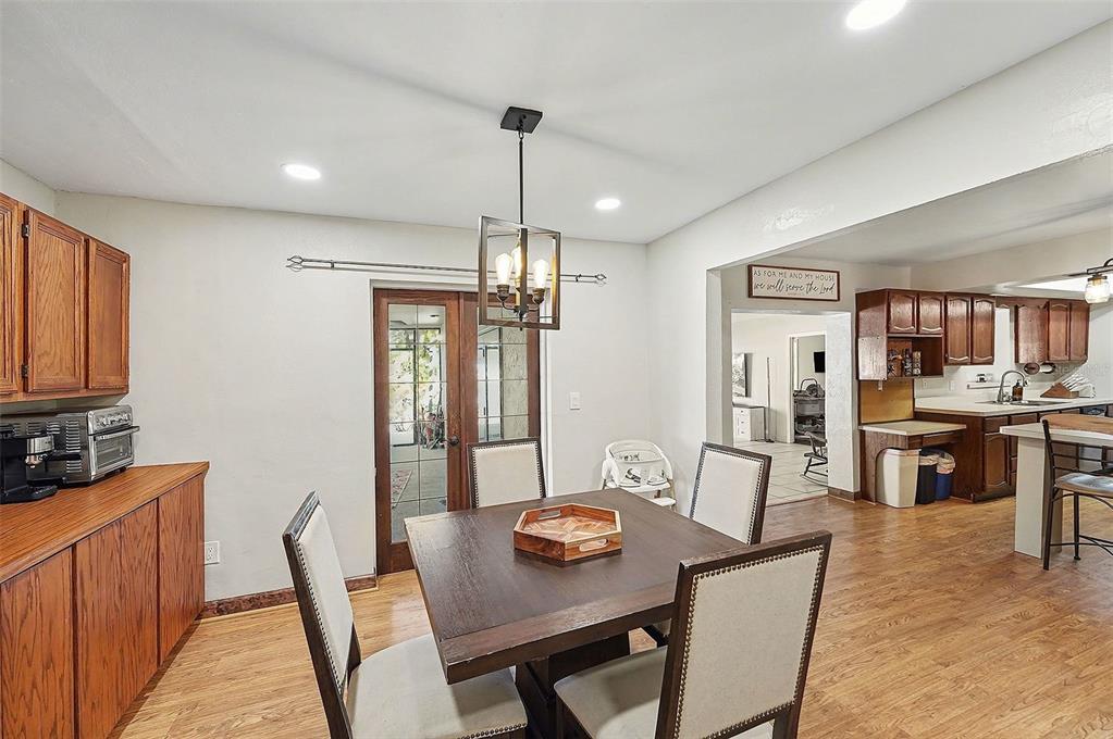 A dining area with a square wooden table and chairs sits adjacent to a kitchen — 5967 102ND AVENUE N, PINELLAS PARK, FL
