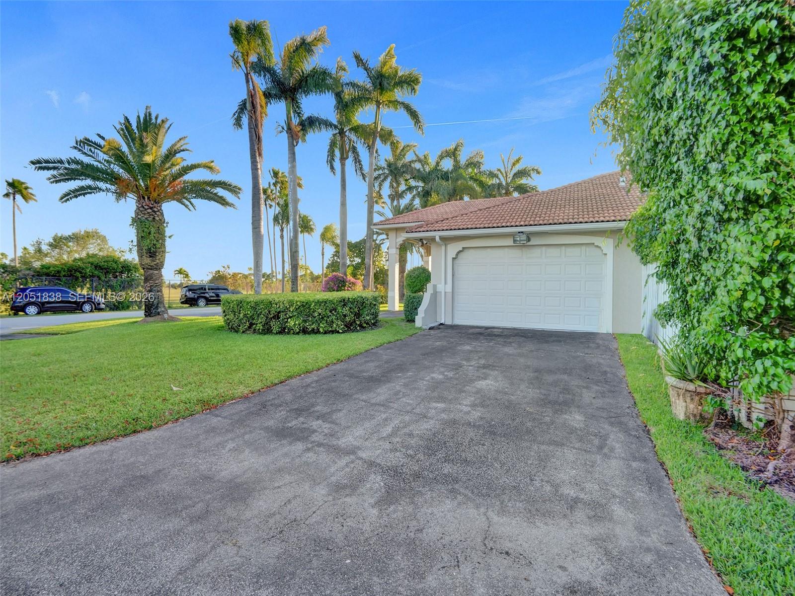 A paved driveway leads to a one-car garage beside a lawn with palm trees — 12401 SW 77th St # 12401, Miami FL 33183, MIAMI, FL