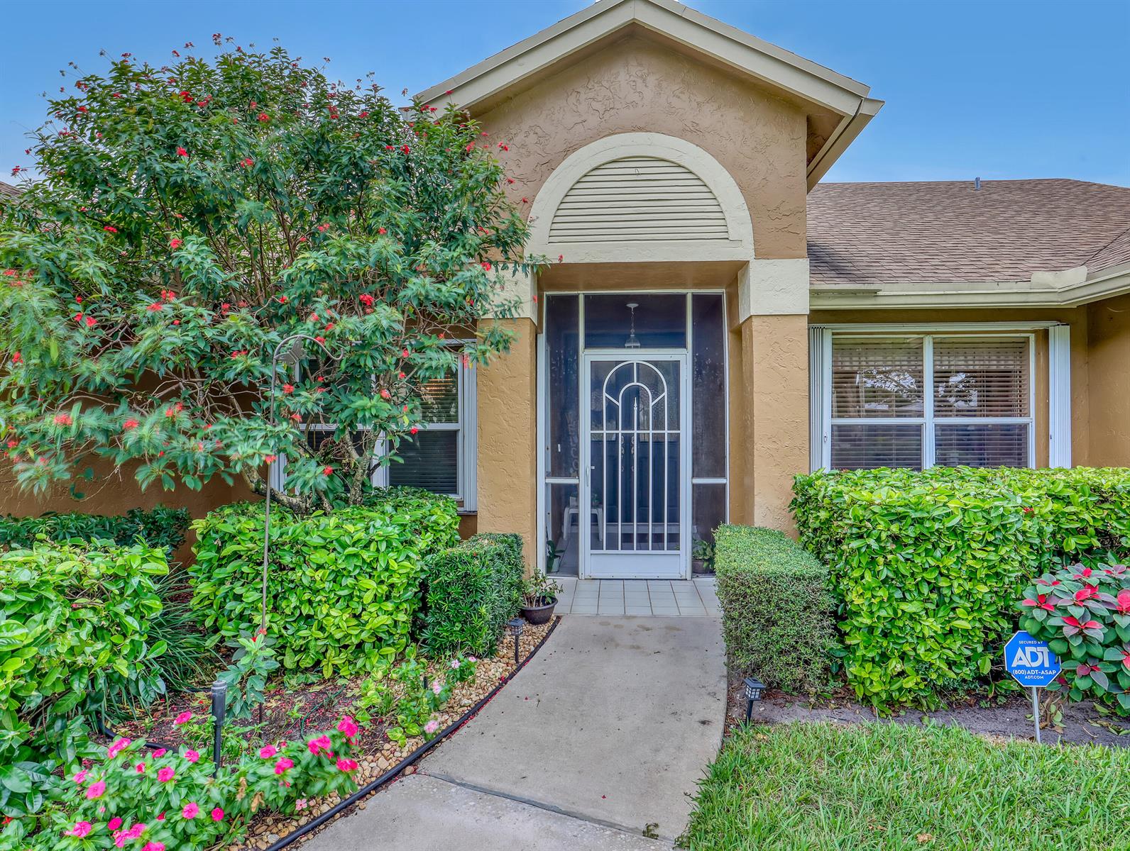 The exterior of a tan house features a front walkway, a screen door, and landscaping — 712 Golf Court, Delray Beach FL 33445, DELRAY BEACH, FL