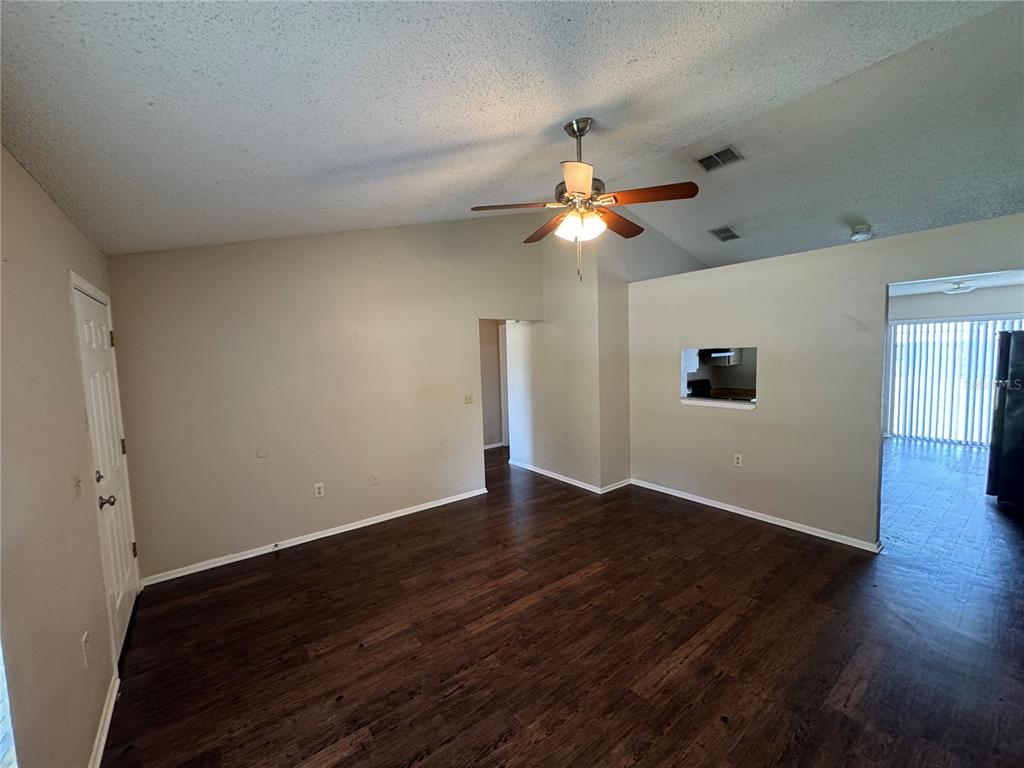 An empty living room features vaulted ceilings, a ceiling fan, and dark wood-look flooring — 10039 MASSEY STREET, ORLANDO, FL