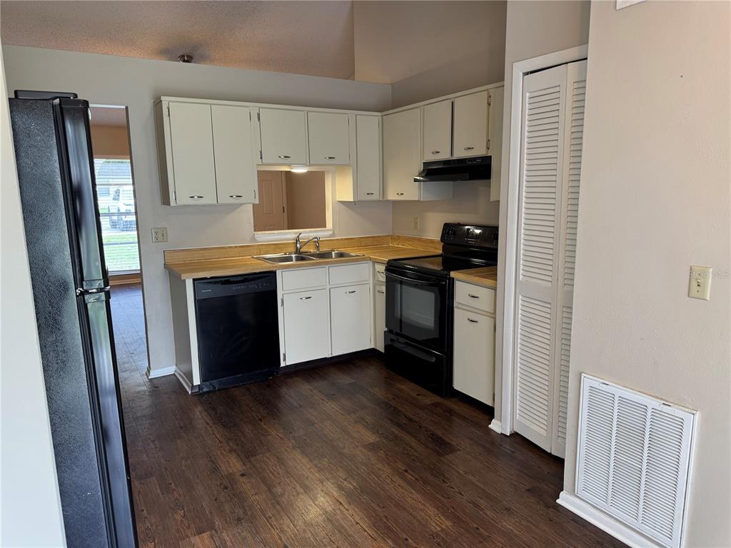 A kitchen features white cabinets, black appliances, a wood-look floor, and a pass-through window — 10039 MASSEY STREET, ORLANDO, FL