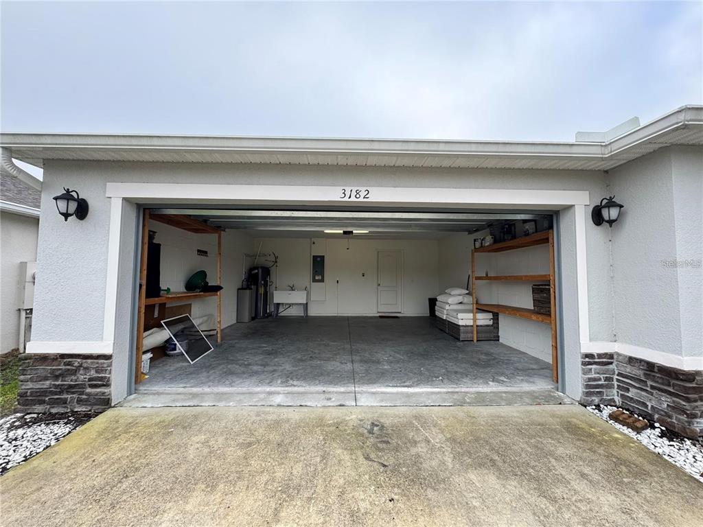 An open two-car garage features concrete floors, built-in wooden shelving, and a utility sink — 3182 EAGLE HAMMOCK CIRCLE, KISSIMMEE, FL