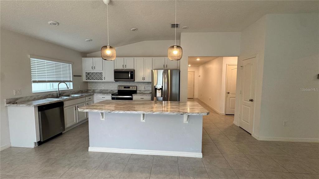 A kitchen features white cabinets, stainless steel appliances, a marble-patterned island, and tile flooring — 3182 EAGLE HAMMOCK CIRCLE, KISSIMMEE, FL