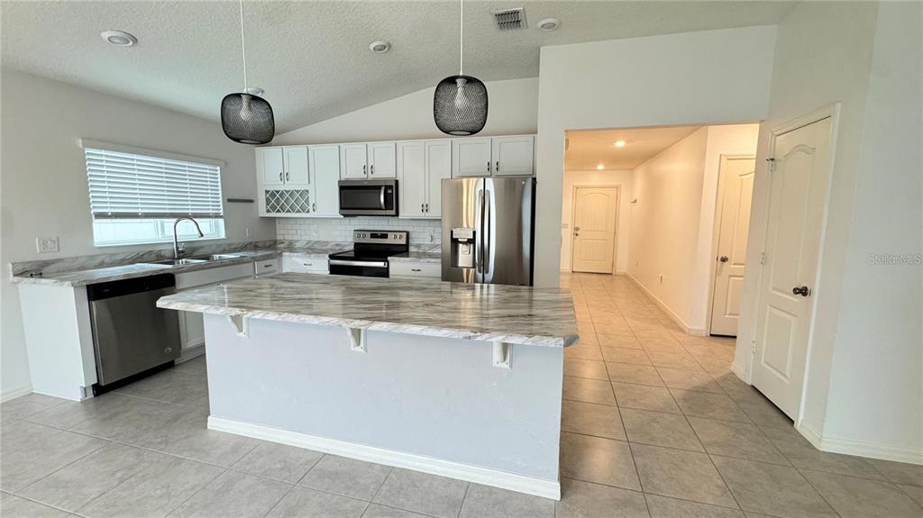 A kitchen features white cabinetry, stainless steel appliances, a marble-patterned island, and tile flooring — 3182 EAGLE HAMMOCK CIRCLE, KISSIMMEE, FL