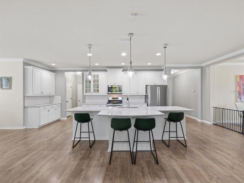A modern kitchen features white cabinetry, a large granite-topped island, and four green bar stools — 740 ROSEMARY CIRCLE, BRADENTON, FL