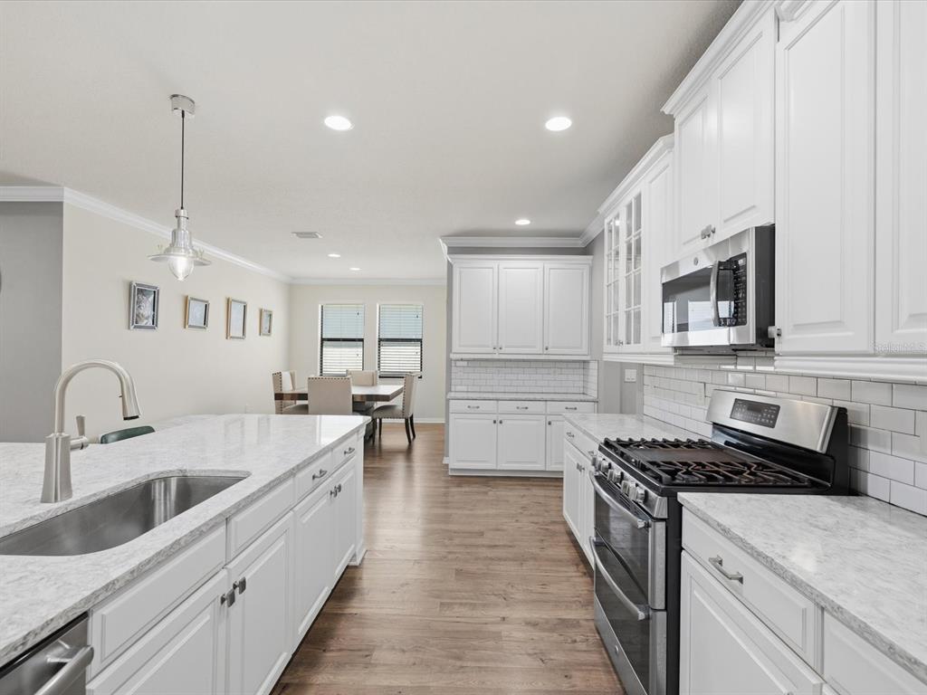 A white kitchen with a marble-topped island and stainless steel appliances opens to a dining area — 740 ROSEMARY CIRCLE, BRADENTON, FL
