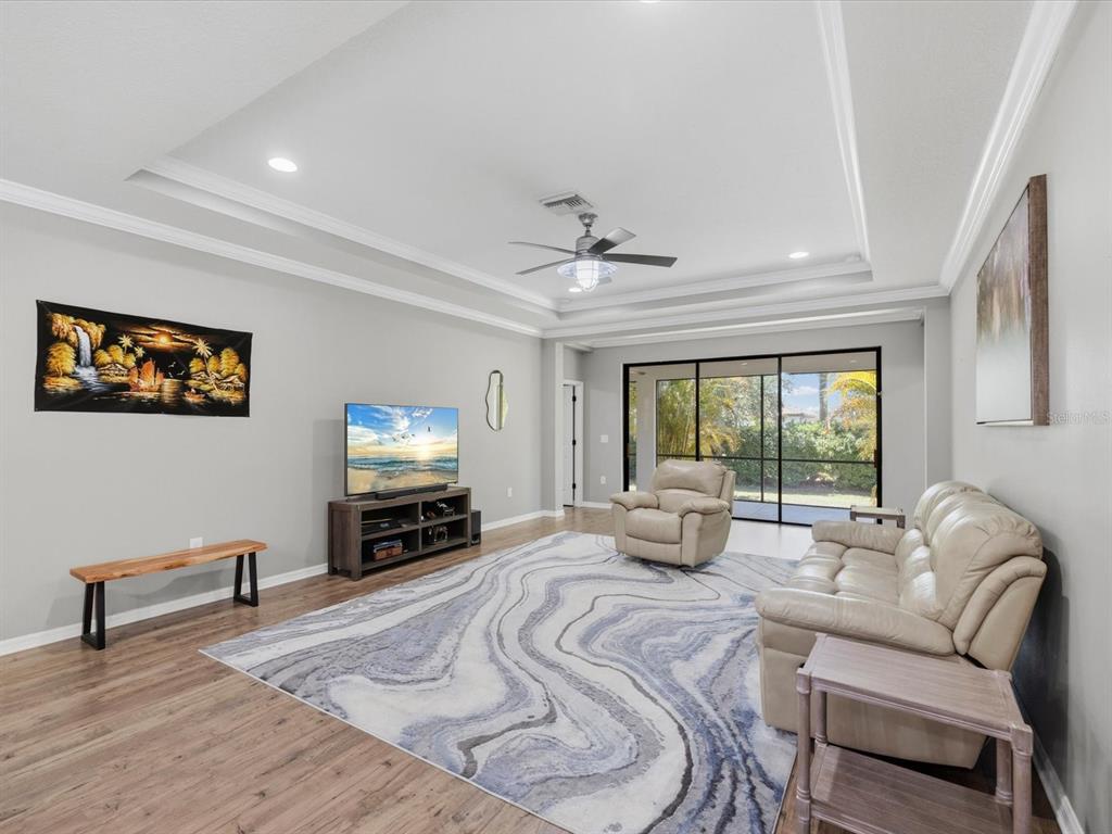 A living room with a tray ceiling, wood-look flooring, a large area rug, and sliding doors — 740 ROSEMARY CIRCLE, BRADENTON, FL