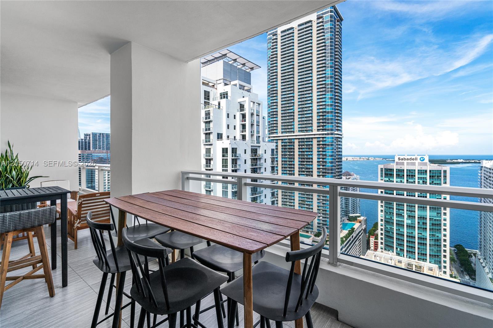 A high-rise balcony features a wooden dining table with chairs overlooking a city skyline — 1080 Brickell Ave # 4102, Miami FL 33131, MIAMI, FL