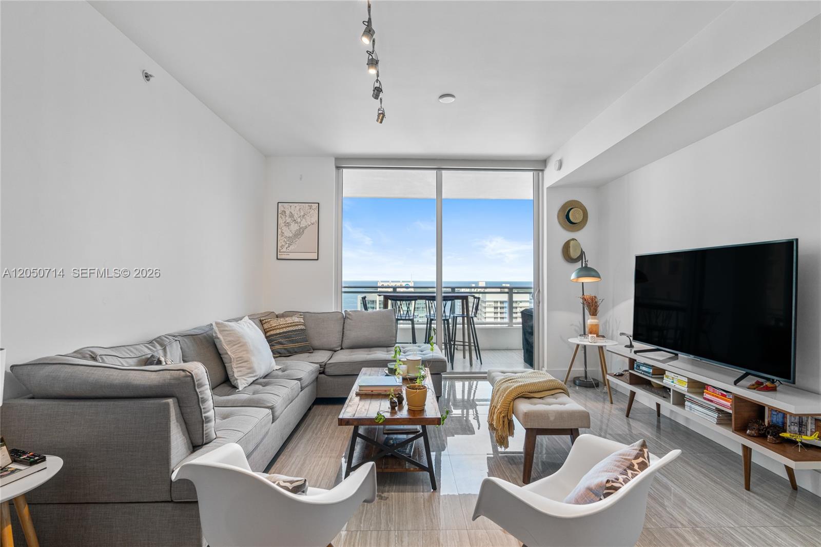 A modern living room features a grey sectional sofa, white accent chairs, and a balcony view — 1080 Brickell Ave # 4102, Miami FL 33131, MIAMI, FL