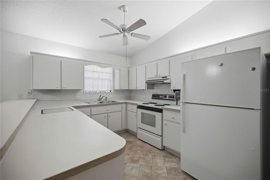 A white kitchen features laminate countertops, white cabinetry, a ceiling fan, and tile flooring — 3925 NE 22ND STREET, OCALA, FL