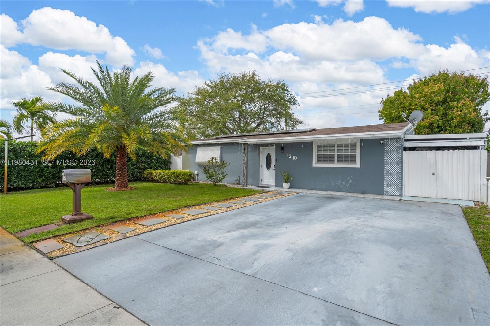 A single-story gray house with a concrete driveway, a palm tree, and a white door — 1210 N 71st Ave, Hollywood FL 33024, HOLLYWOOD, FL