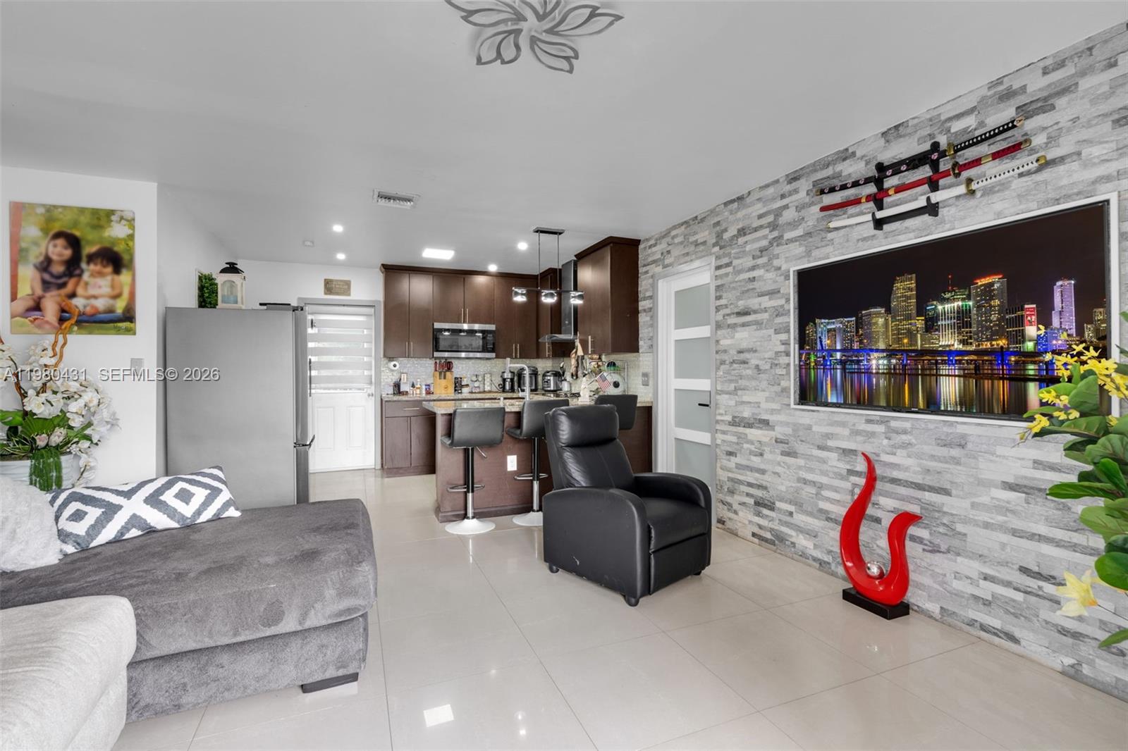 A living room and kitchen area features a stone accent wall, television, and leather recliner — 1210 N 71st Ave, Hollywood FL 33024, HOLLYWOOD, FL