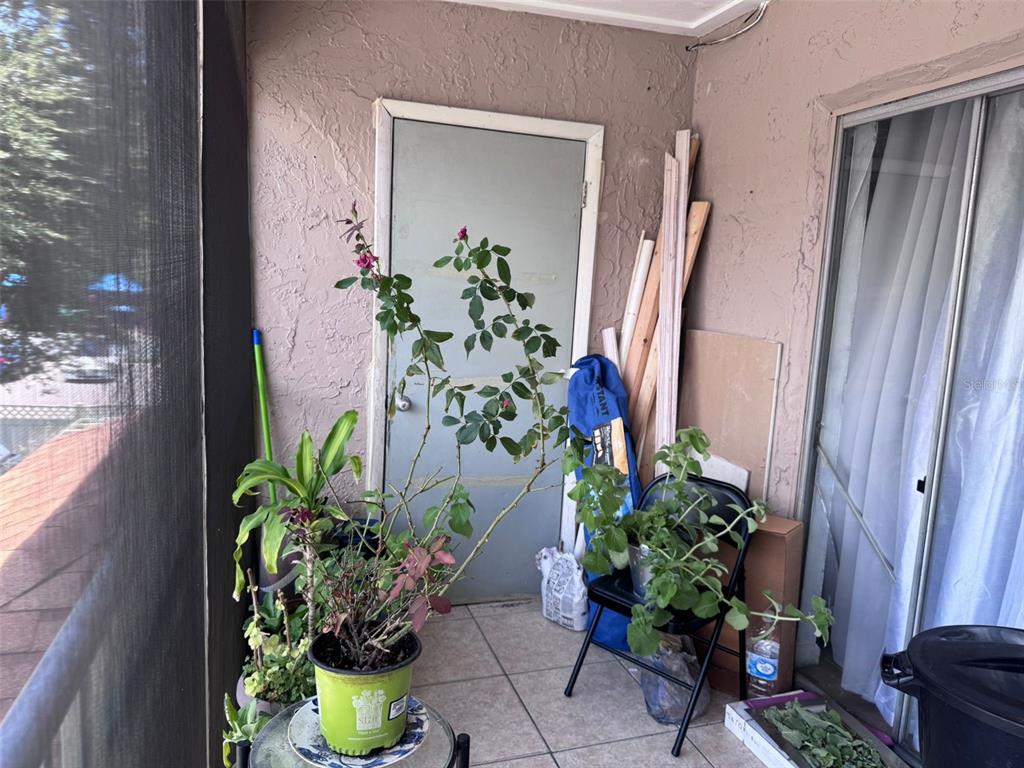 A covered balcony features a rose plant, a potted shrub, a folding chair, and construction materials — 7210 N MANHATTAN AVENUE UNIT 2423, TAMPA, FL