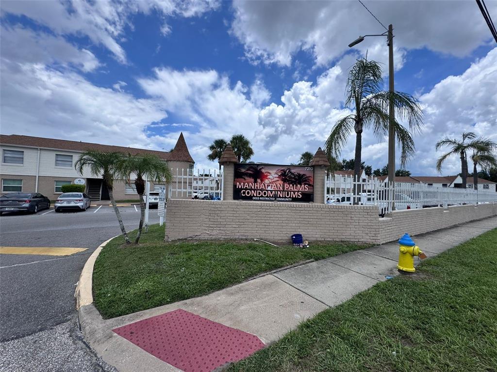 A brick sign for Manhattan Palms Condominiums stands near a parking lot and sidewalk — 7210 N MANHATTAN AVENUE UNIT 2423, TAMPA, FL