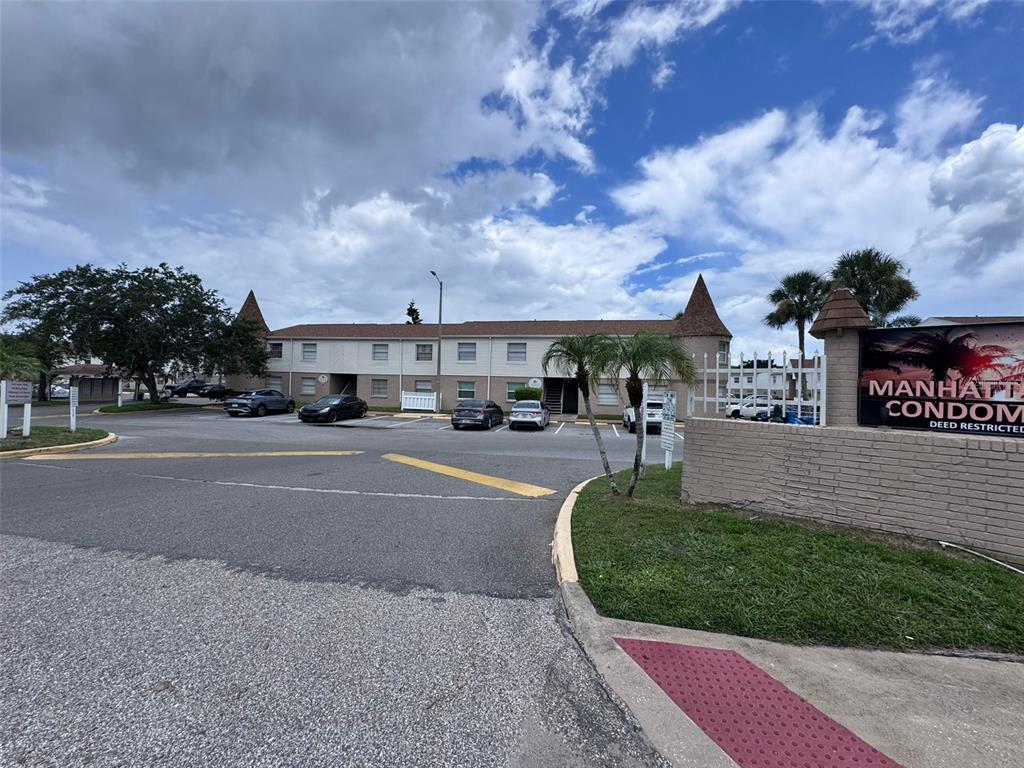 A multi-story apartment building with a parking lot and a sign in the foreground — 7210 N MANHATTAN AVENUE UNIT 2423, TAMPA, FL