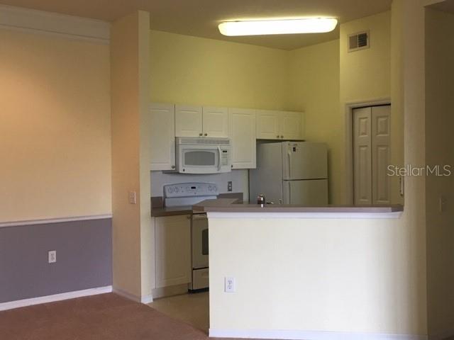 A kitchen with white cabinets, a microwave, and a refrigerator overlooks a living area — 5180 NORTHRIDGE ROAD UNIT 308, SARASOTA, FL