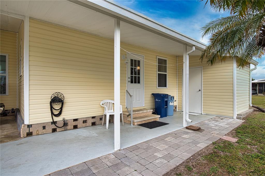 A covered concrete patio with light yellow siding, a white door, and a brick walkway — 618 IGLESIA DRIVE, NORTH PORT, FL