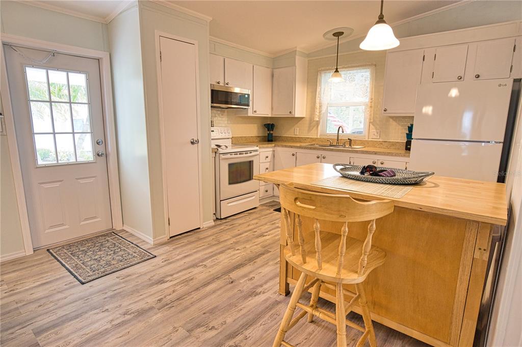 A kitchen features white cabinets, light wood-look flooring, a central island, and a white refrigerator — 618 IGLESIA DRIVE, NORTH PORT, FL