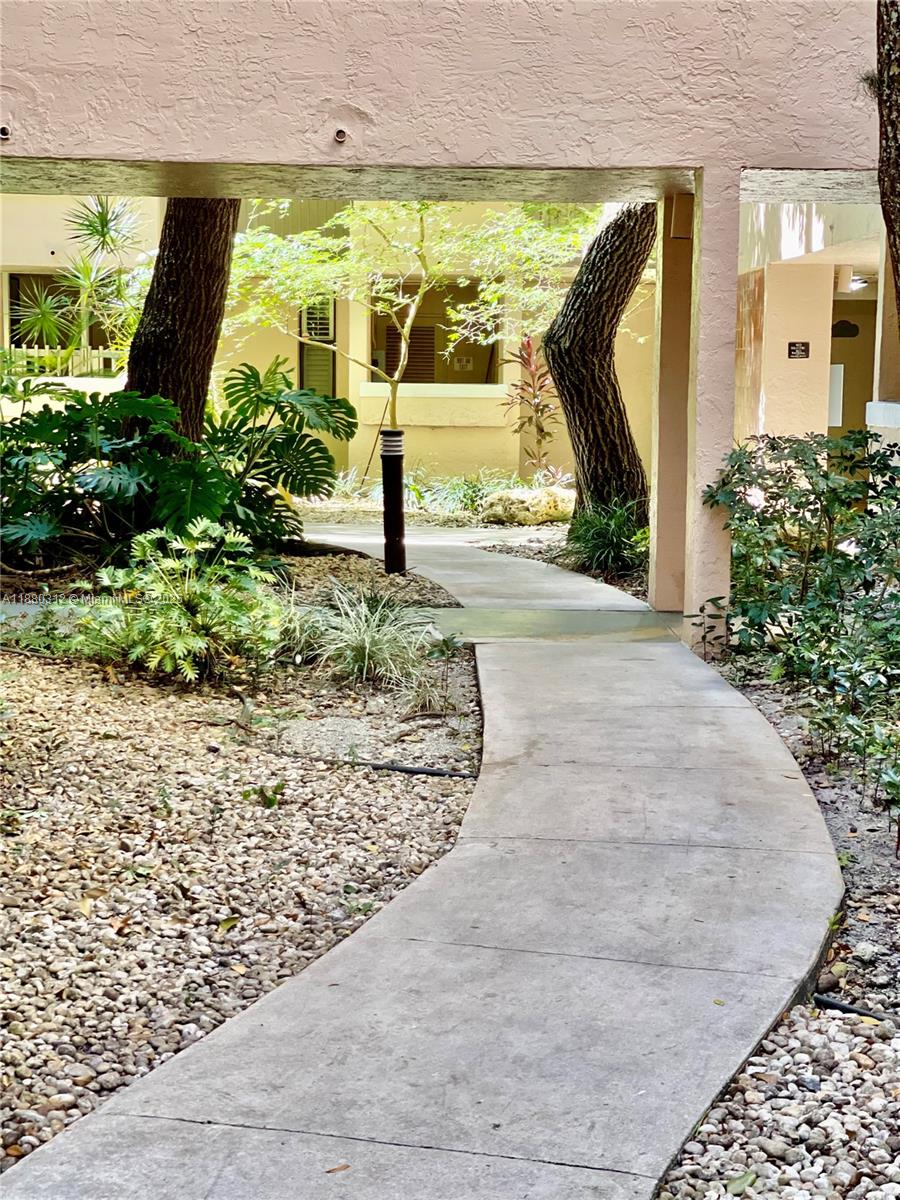 A concrete walkway leads through a landscaped courtyard between two residential buildings — 6800 Cypress Rd # 408, Plantation FL 33317, PLANTATION, FL