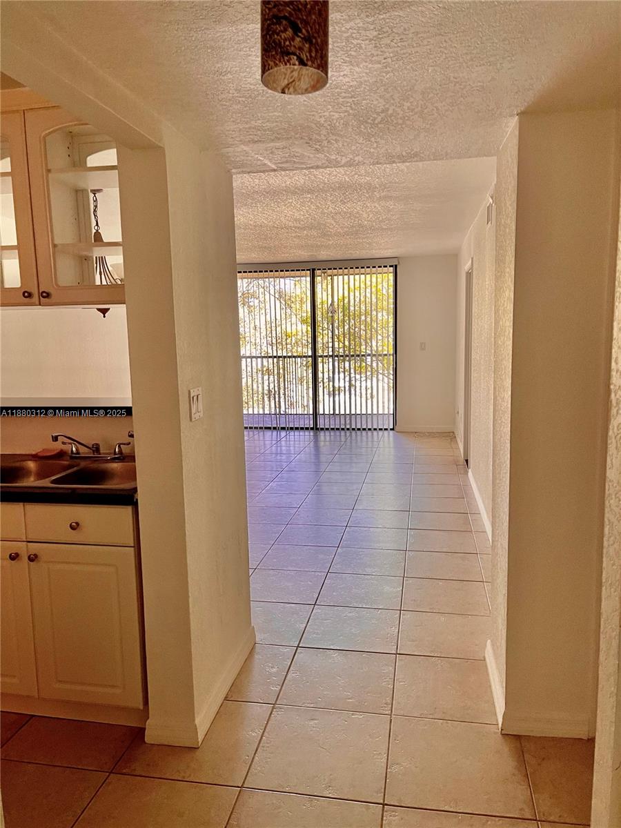 A tiled hallway leads from a kitchen toward a living area with sliding glass doors — 6800 Cypress Rd # 408, Plantation FL 33317, PLANTATION, FL