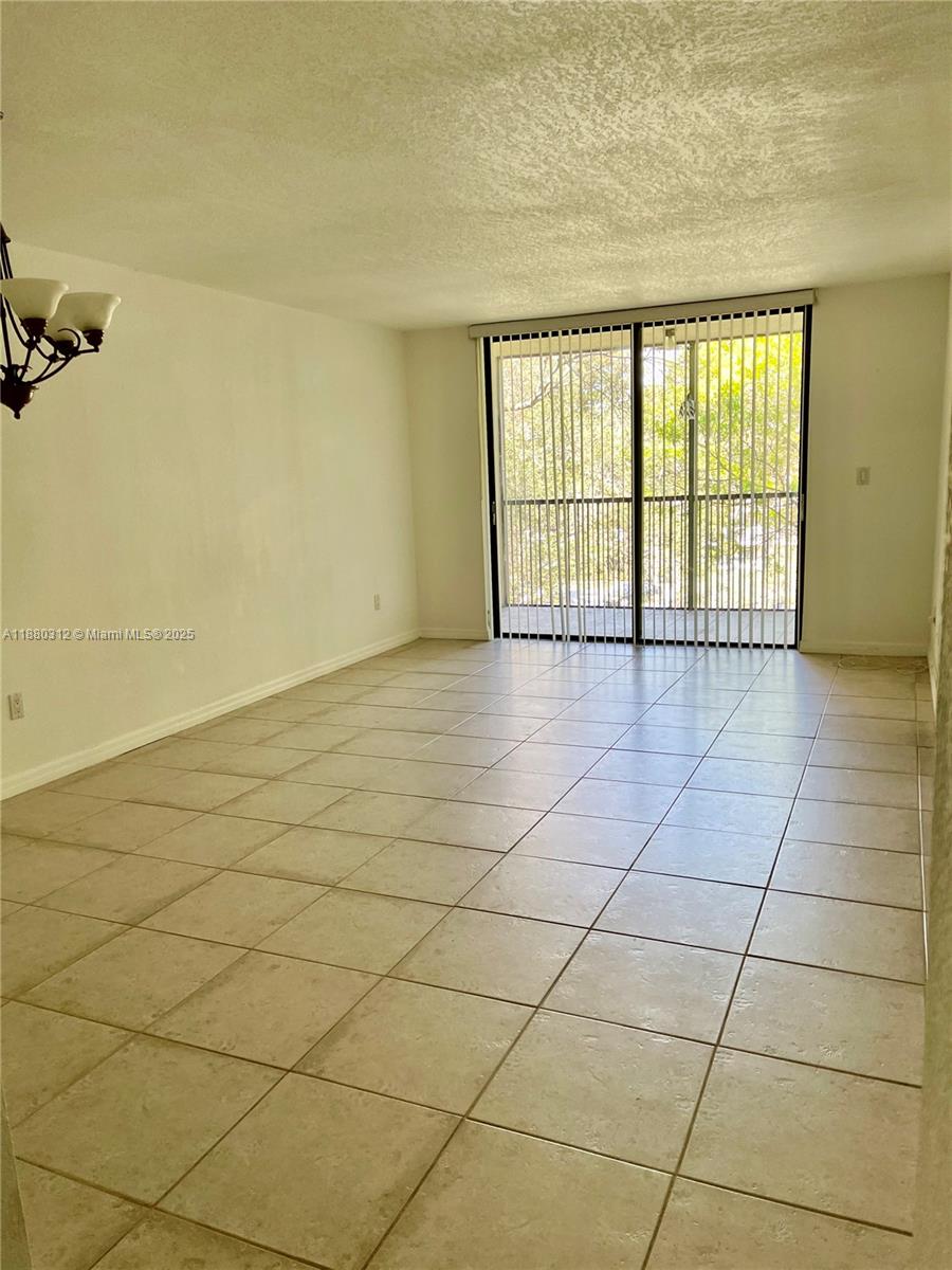 An empty living room features light-colored tile flooring and a sliding glass door to a balcony — 6800 Cypress Rd # 408, Plantation FL 33317, PLANTATION, FL