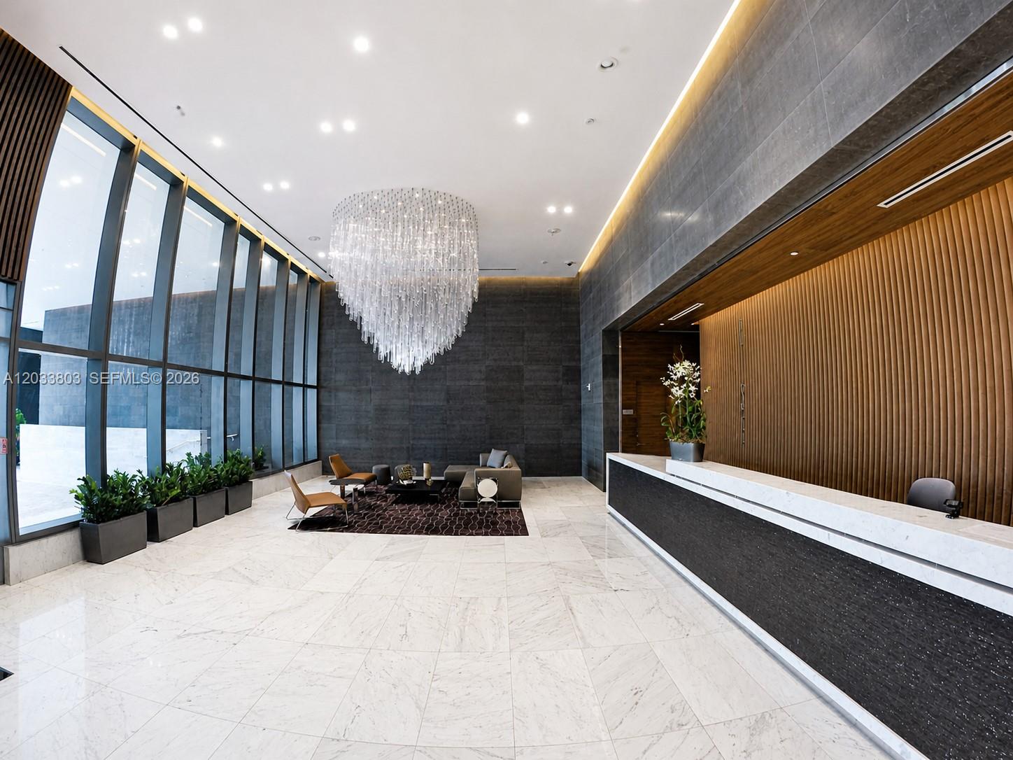 A modern lobby features a large crystal chandelier, marble floors, and a wood-paneled reception desk — 88 SW 7th St # 2206, Miami FL 33130, MIAMI, FL