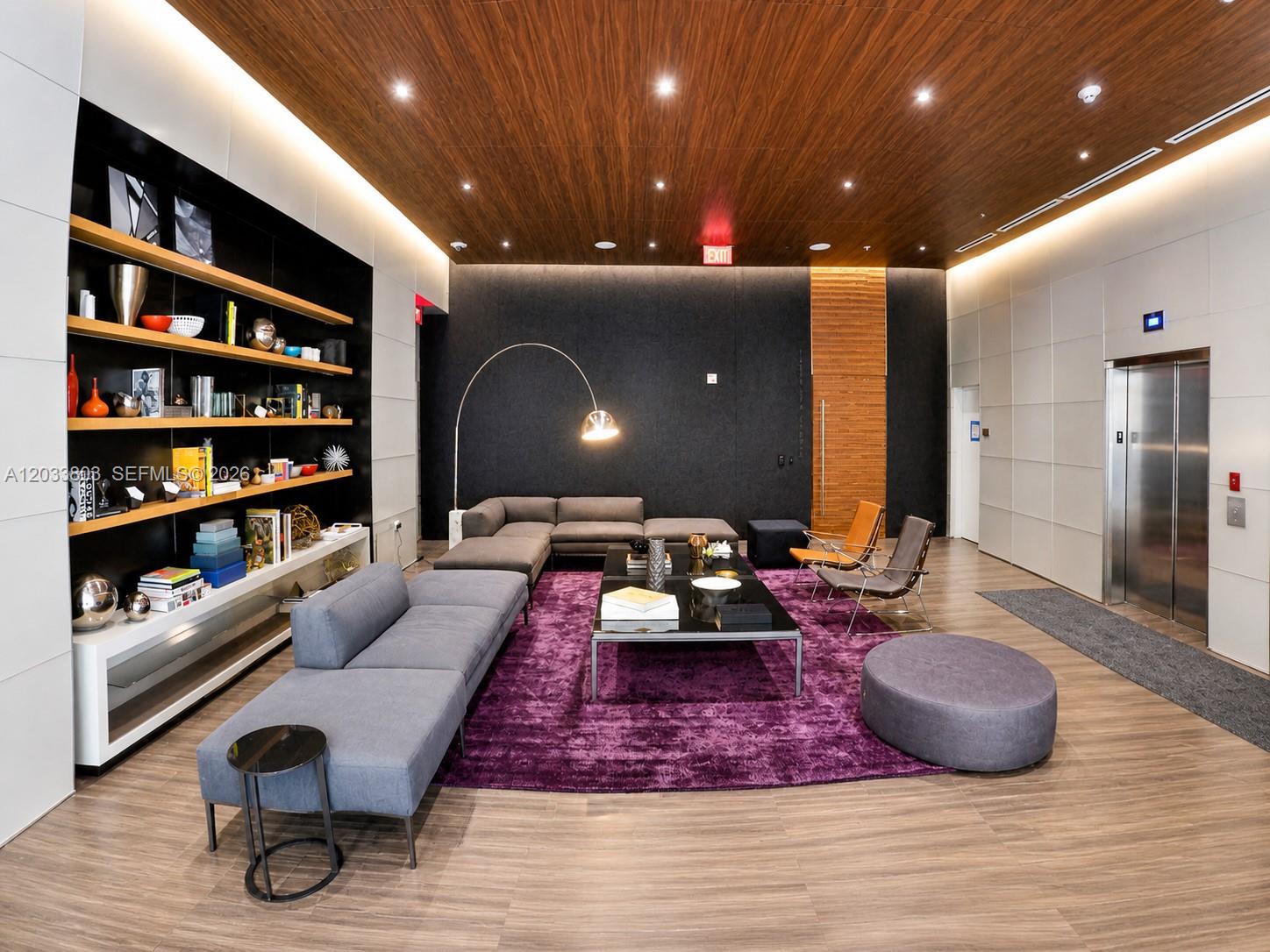 A modern lounge features a purple rug, gray sectional sofas, wood-paneled ceiling, and built-in shelving — 88 SW 7th St # 2206, Miami FL 33130, MIAMI, FL