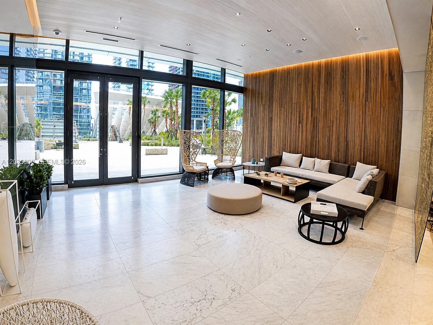A modern lobby features a wood-paneled wall, marble floors, and floor-to-ceiling windows overlooking a courtyard — 88 SW 7th St # 2206, Miami FL 33130, MIAMI, FL