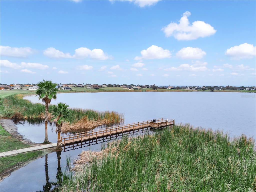 A wooden pier extends into a lake surrounded by tall grass and residential homes — 429 ADAMS VIEW LANE, AUBURNDALE, FL