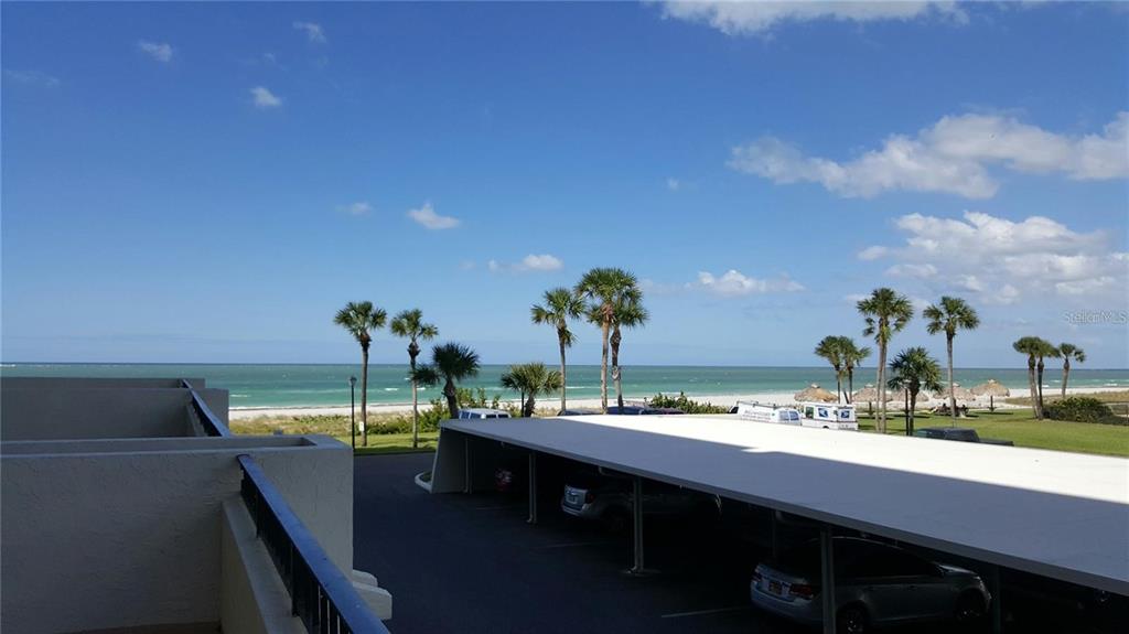 An elevated view shows a parking carport, palm trees, and a sandy beach by the ocean — 1480 GULF BOULEVARD UNIT 106, CLEARWATER BEACH, FL