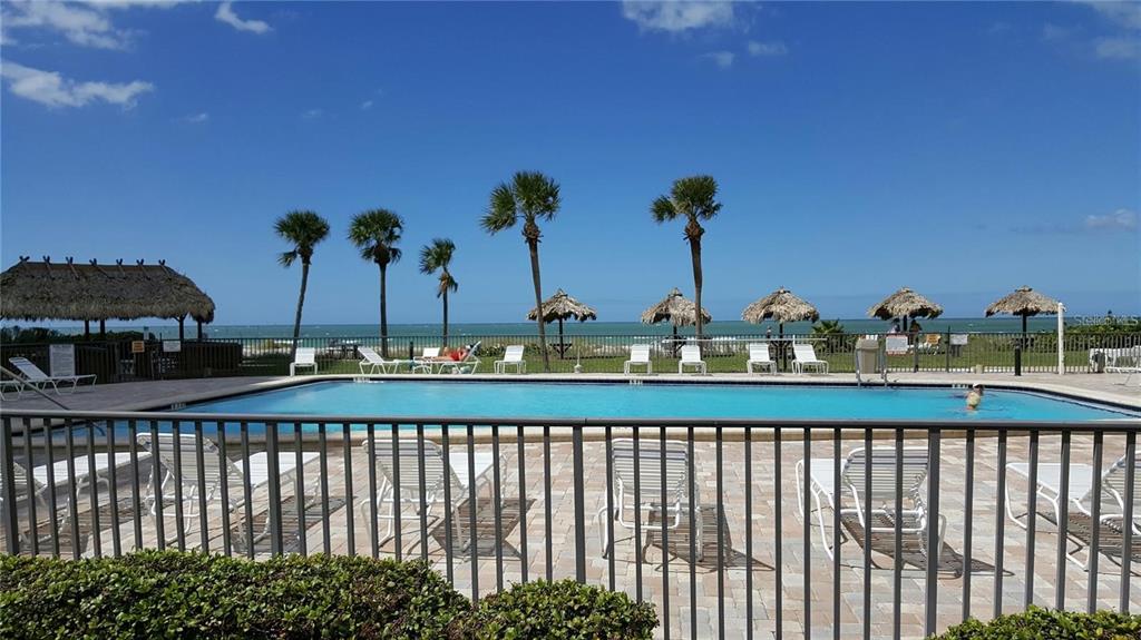 A swimming pool overlooks the ocean with palm trees and thatched umbrellas on the beach — 1480 GULF BOULEVARD UNIT 106, CLEARWATER BEACH, FL