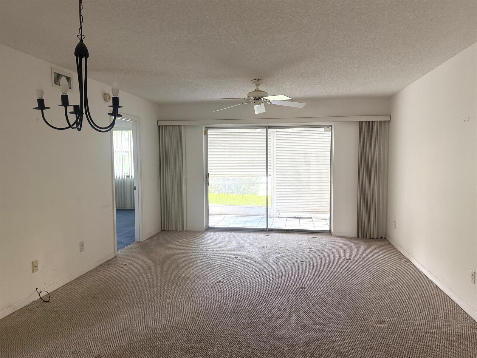 An empty living room features beige carpeting, a ceiling fan, and sliding glass patio doors — 10382 NW 24th Place, Sunrise FL 33322, SUNRISE, FL