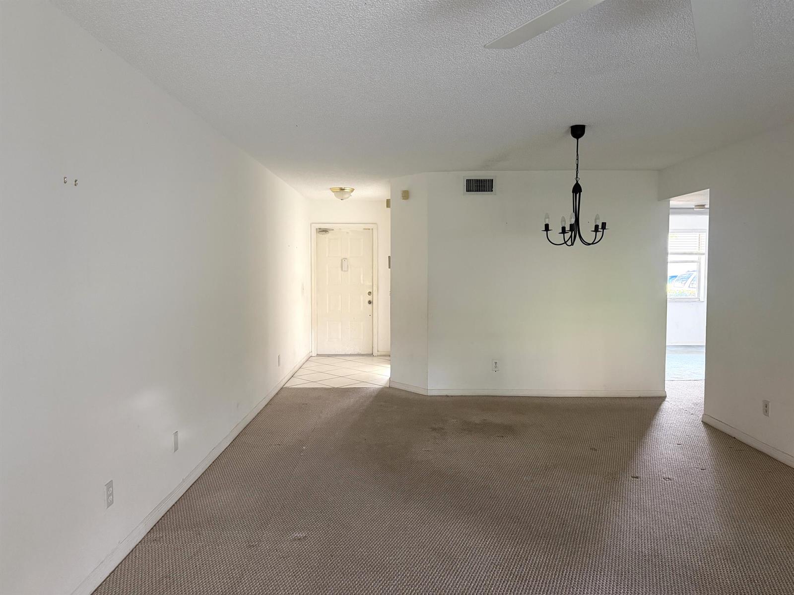 An empty room features beige carpeting, white walls, a dining chandelier, and an entryway door — 10382 NW 24th Place, Sunrise FL 33322, SUNRISE, FL