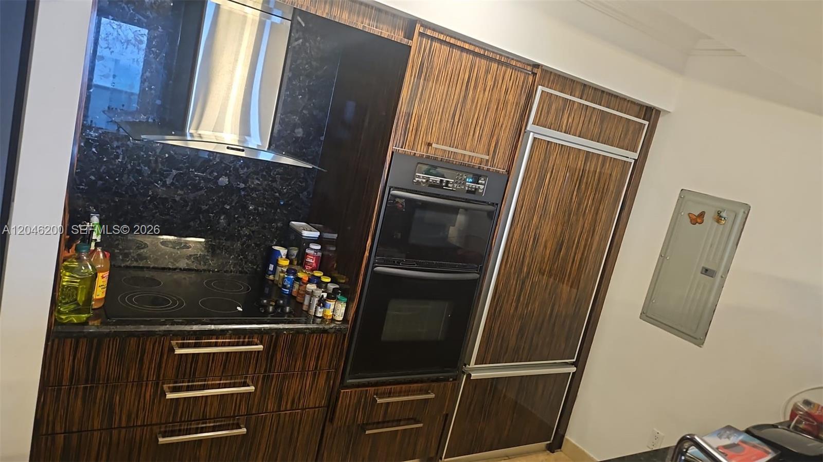 A modern kitchen features dark wood-grain cabinetry, a black granite backsplash, and built-in stainless appliances — 1830 S Ocean Dr # 2403, Hallandale Beach FL 33009, HALLANDALE BEACH, FL