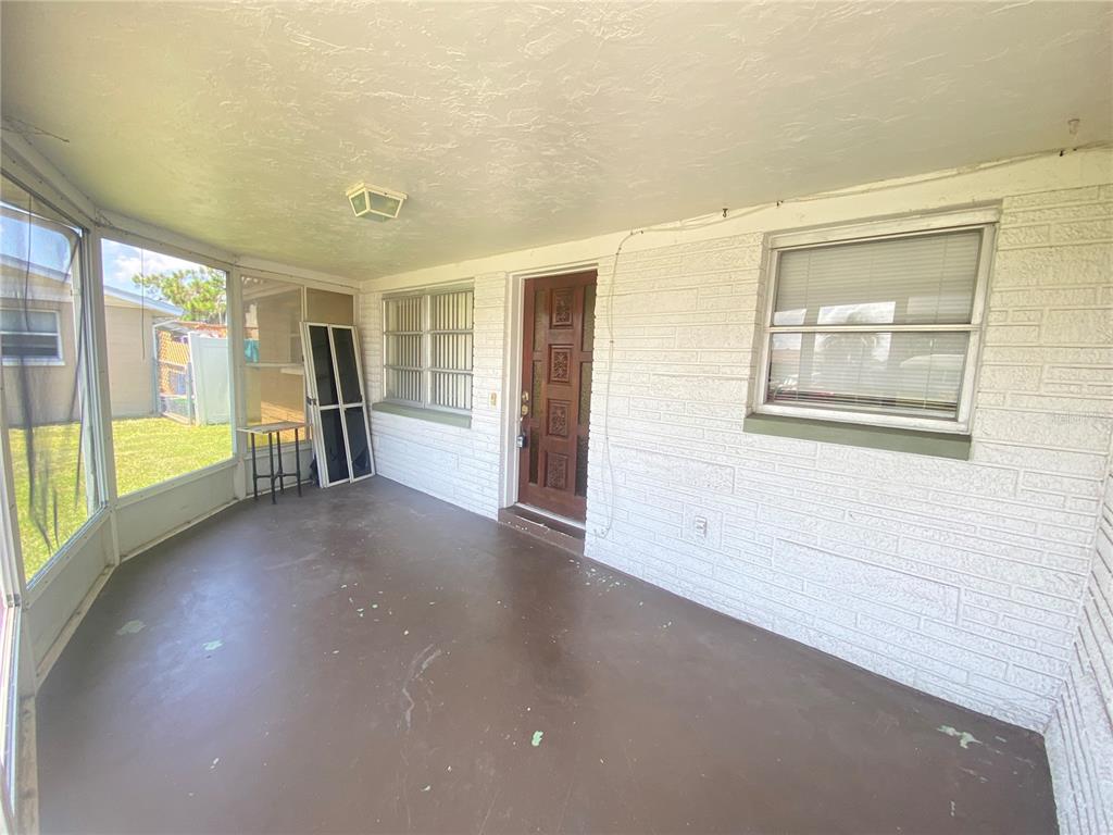 A covered patio with a brown floor, white brick walls, and a wooden front door — 2713 CAPRICORN PLACE, HOLIDAY, FL