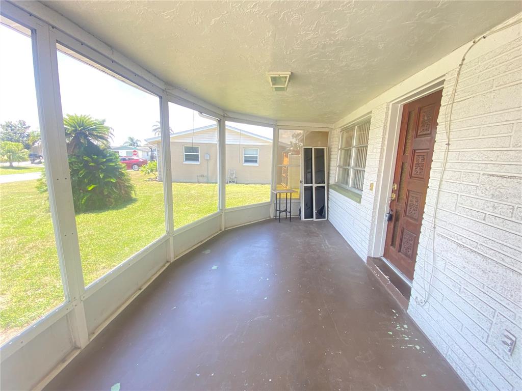 A screened-in porch with a concrete floor, white brick wall, and a wooden front door — 2713 CAPRICORN PLACE, HOLIDAY, FL