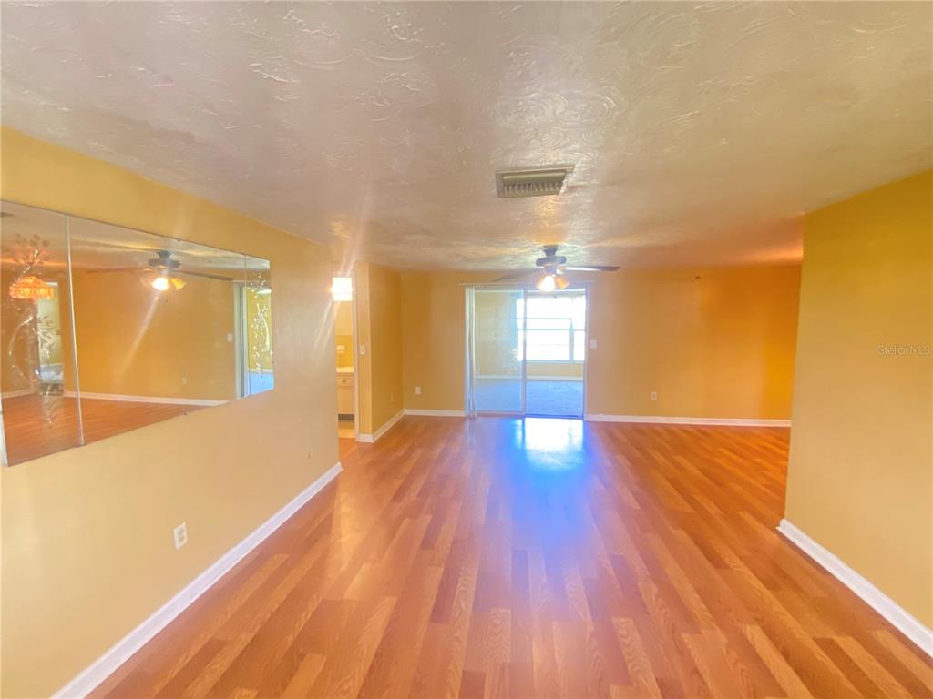An interior view of a living room with yellow walls, wood flooring, and a mirrored wall — 2713 CAPRICORN PLACE, HOLIDAY, FL