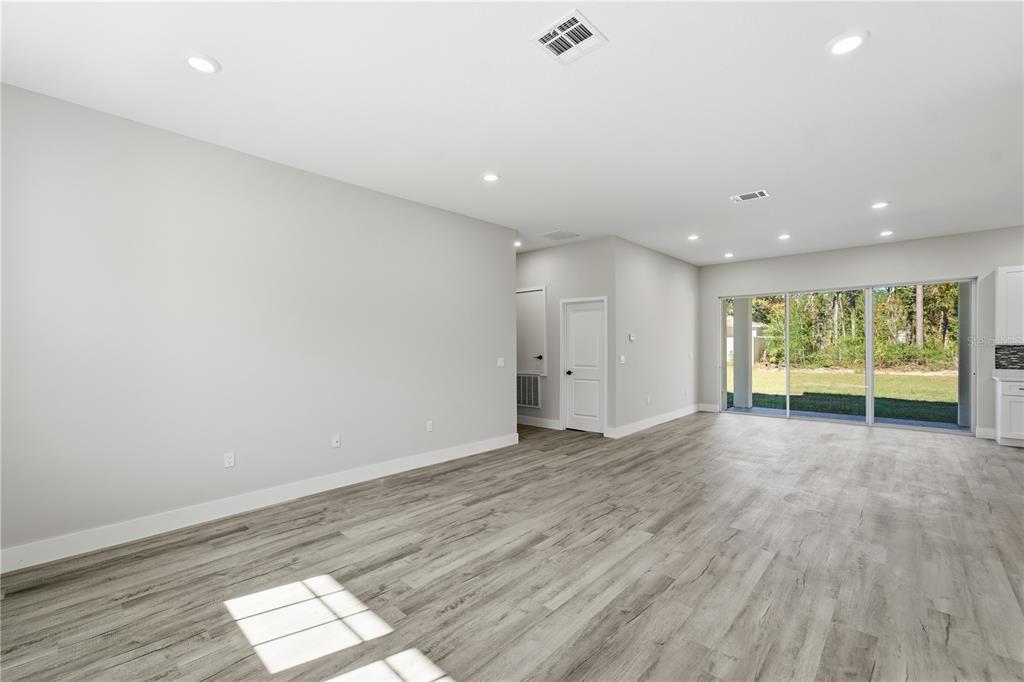 An open-concept living area features light gray walls, wood-look flooring, recessed lighting, and sliding glass doors — 13205 SW 65TH CIRCLE, OCALA, FL