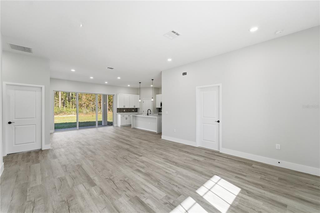 An open-concept living area features light wood-look flooring, white walls, and a kitchen with island — 13205 SW 65TH CIRCLE, OCALA, FL