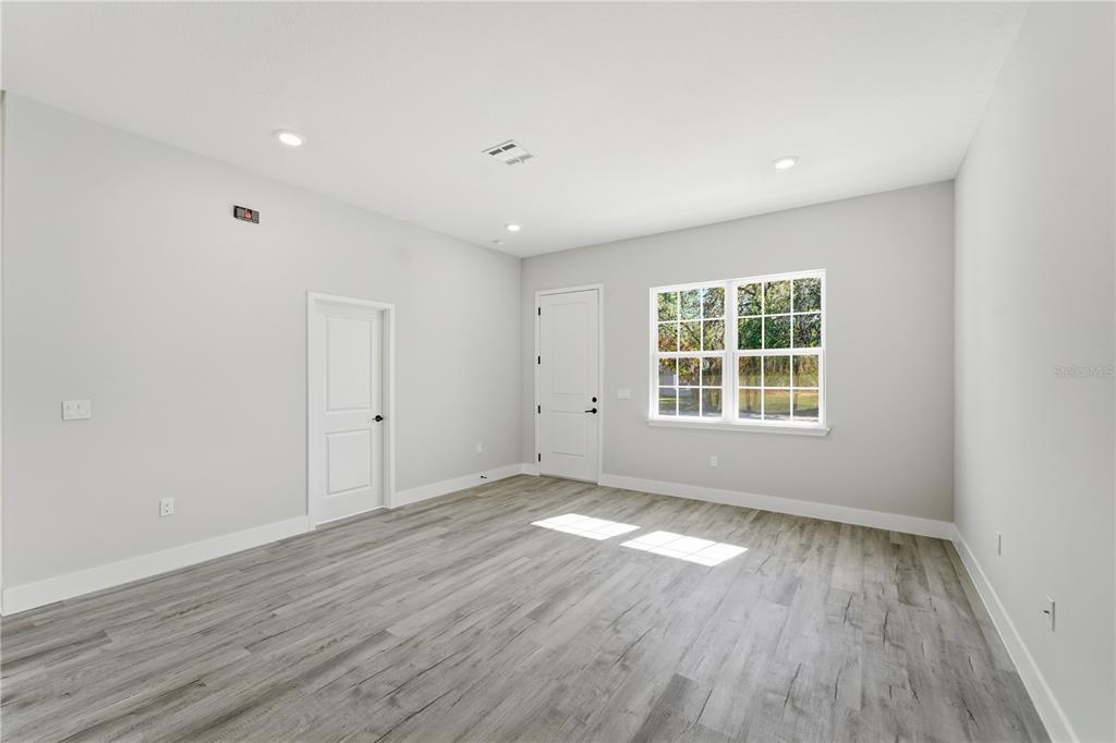 An empty room with light gray walls, wood-look flooring, two white doors, and a window — 13205 SW 65TH CIRCLE, OCALA, FL