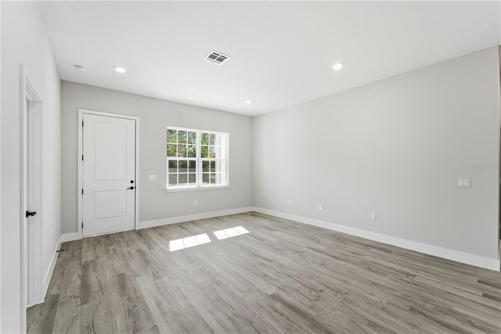 A bright, empty room features light gray walls, wood-look flooring, a window, and a door — 13205 SW 65TH CIRCLE, OCALA, FL