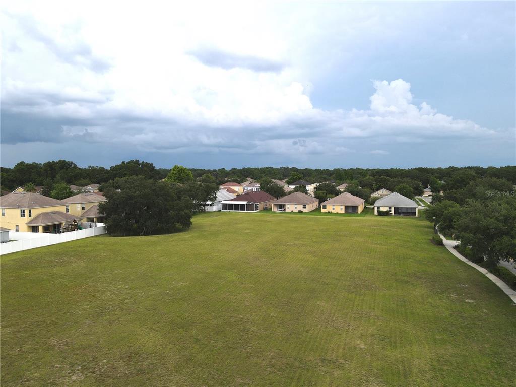 An aerial view shows a large, grassy vacant lot surrounded by suburban houses and trees — 1035 NASHVILLE DRIVE, WESLEY CHAPEL, FL