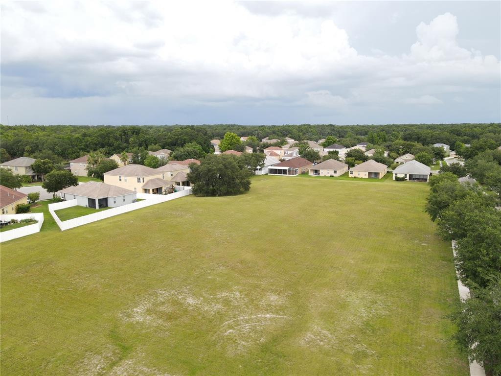 An aerial view shows a large, grassy vacant lot surrounded by suburban residential houses — 1035 NASHVILLE DRIVE, WESLEY CHAPEL, FL