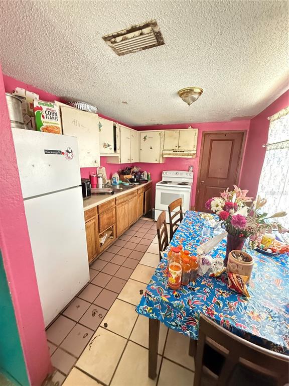 A kitchen features pink walls, wood cabinets, a white refrigerator, and a floral-covered dining table — 4212 9TH STREET E, BRADENTON, FL