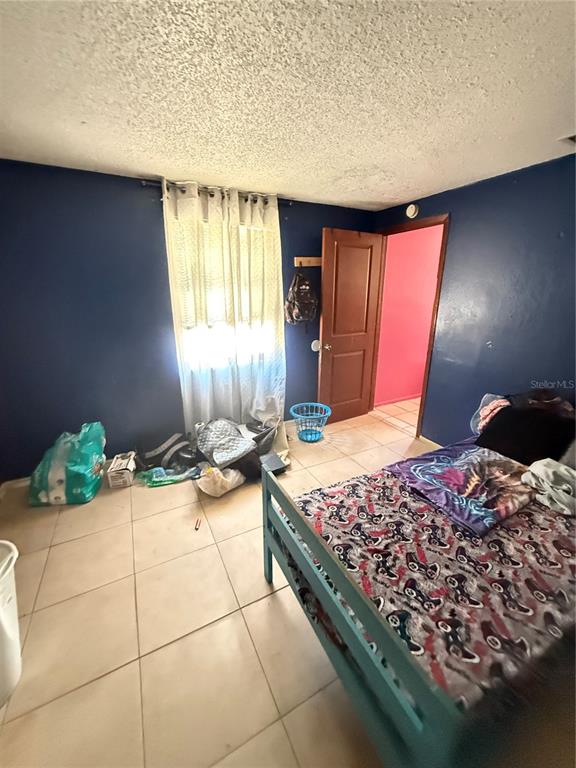 A bedroom with dark blue walls, a bed, a window with curtains, and tile flooring — 4212 9TH STREET E, BRADENTON, FL