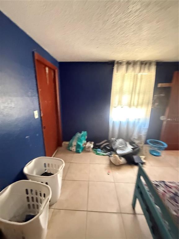 A bedroom with blue walls, tile flooring, two laundry baskets, and a window with curtains — 4212 9TH STREET E, BRADENTON, FL
