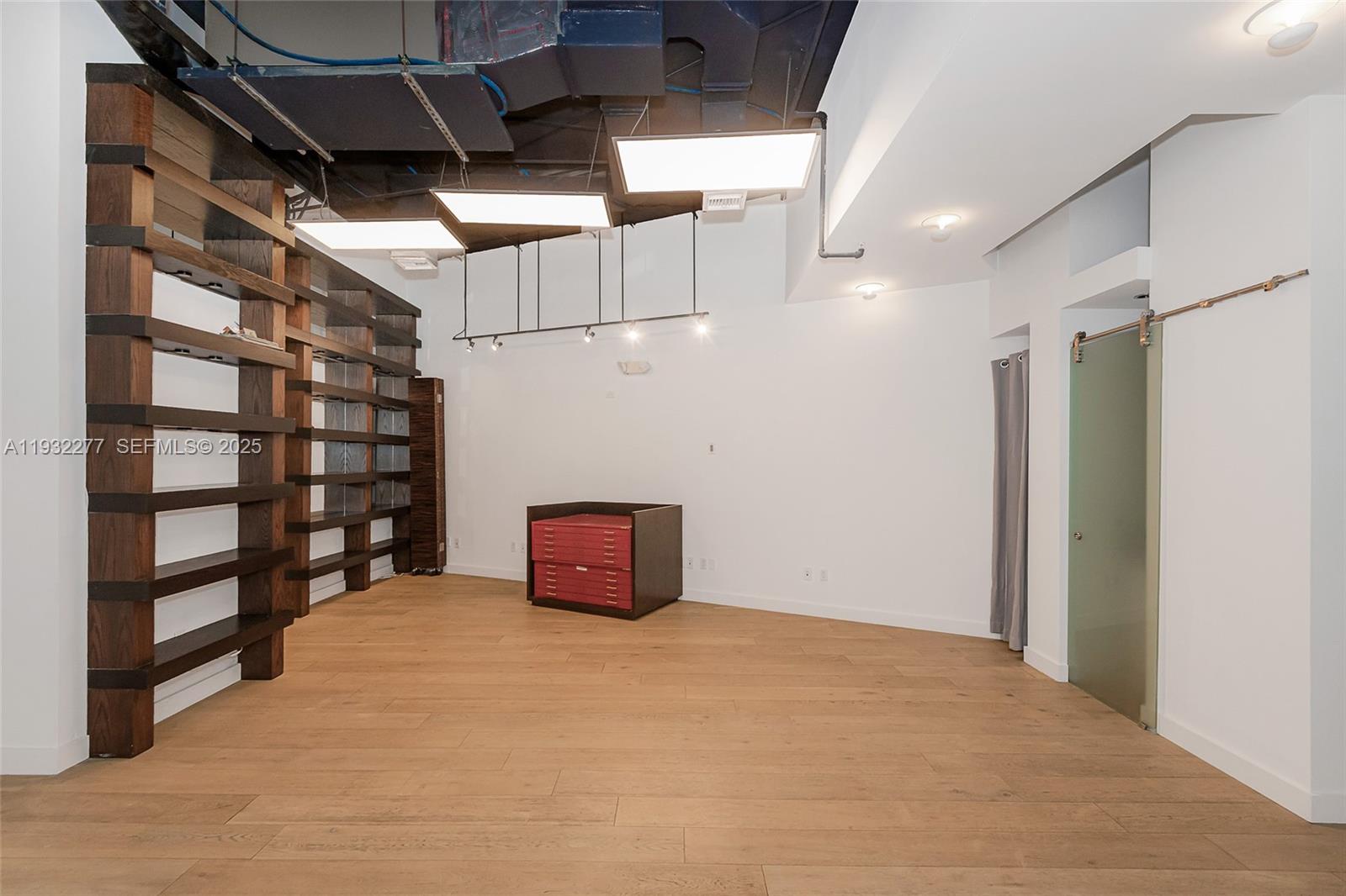 An open room features wood shelving, light wood flooring, and exposed industrial ceiling elements — 2030 S Douglas Rd # 120, Coral Gables FL 33134, CORAL GABLES, FL