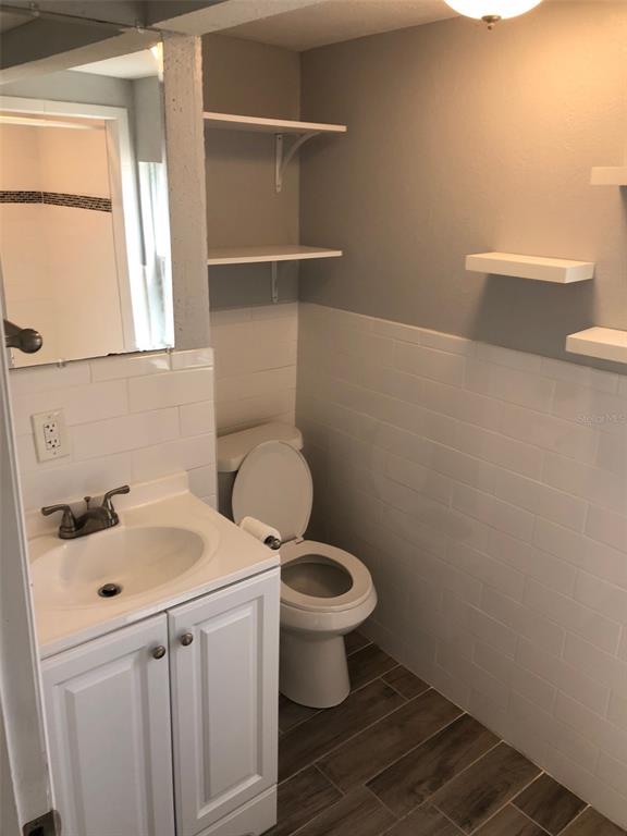 A small bathroom features a white vanity, a toilet, subway tile walls, and floating shelves — 216 12TH AVENUE N UNIT Downstairs, ST PETERSBURG, FL
