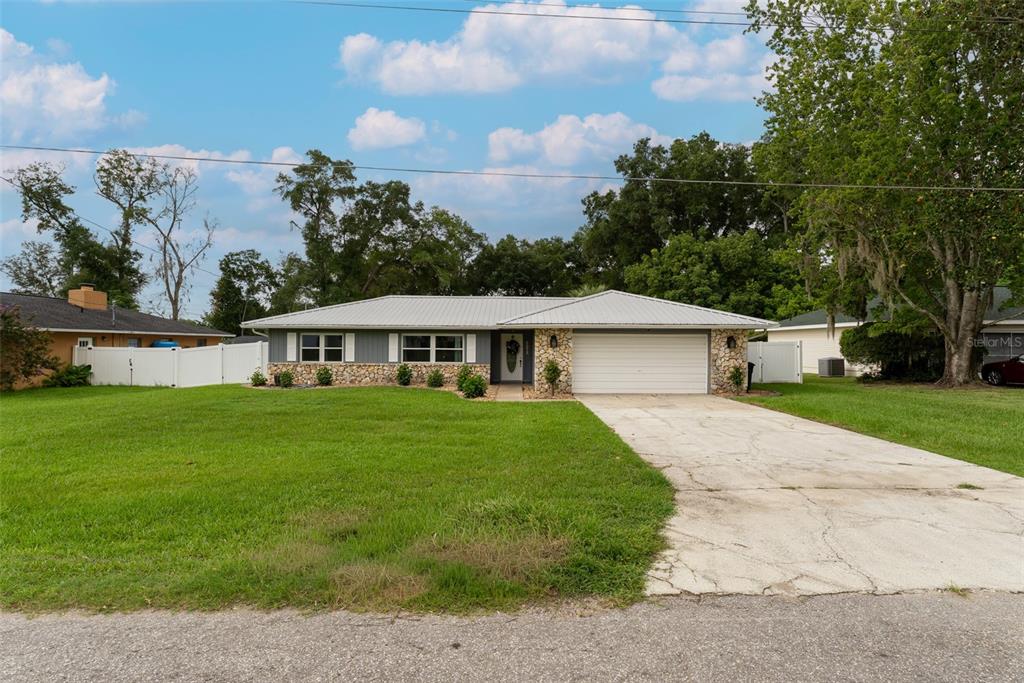 A single-story house with a metal roof, stone accents, and a concrete driveway — 5072 SE 27TH STREET, OCALA, FL